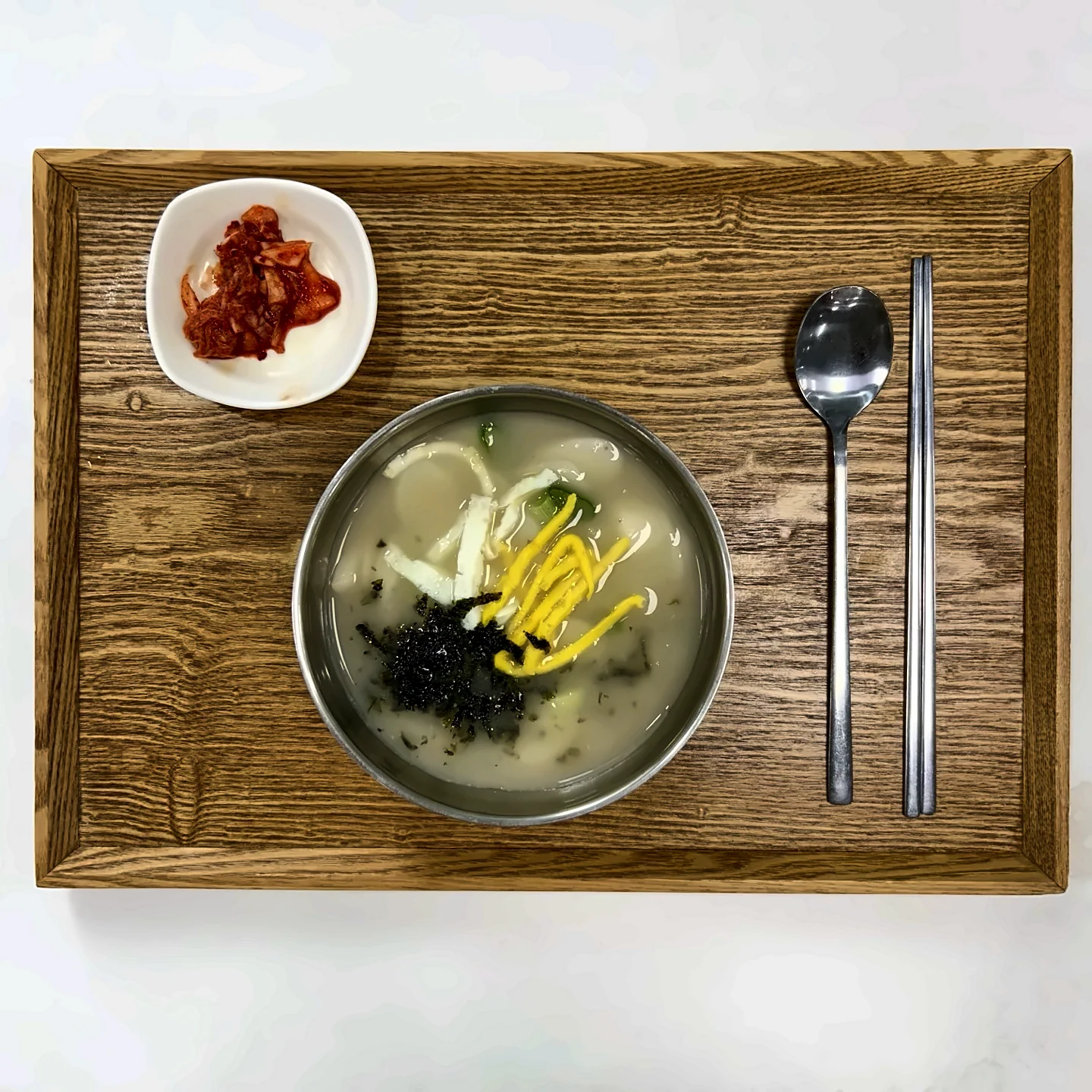 나무 쟁반에 차린 떡국. 계란 지단과 김 가루를 올리고 김치를 곁들였습니다