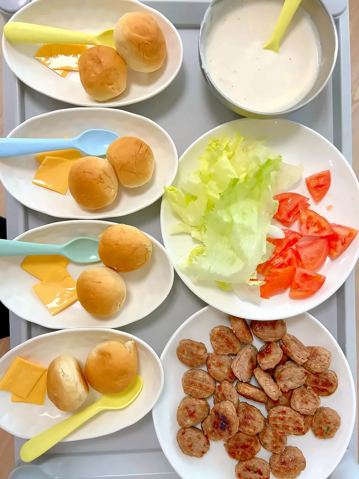 쟁반 위 접시마다 나눠 담은 작은 빵, 치즈, 양상추, 토마토, 패티