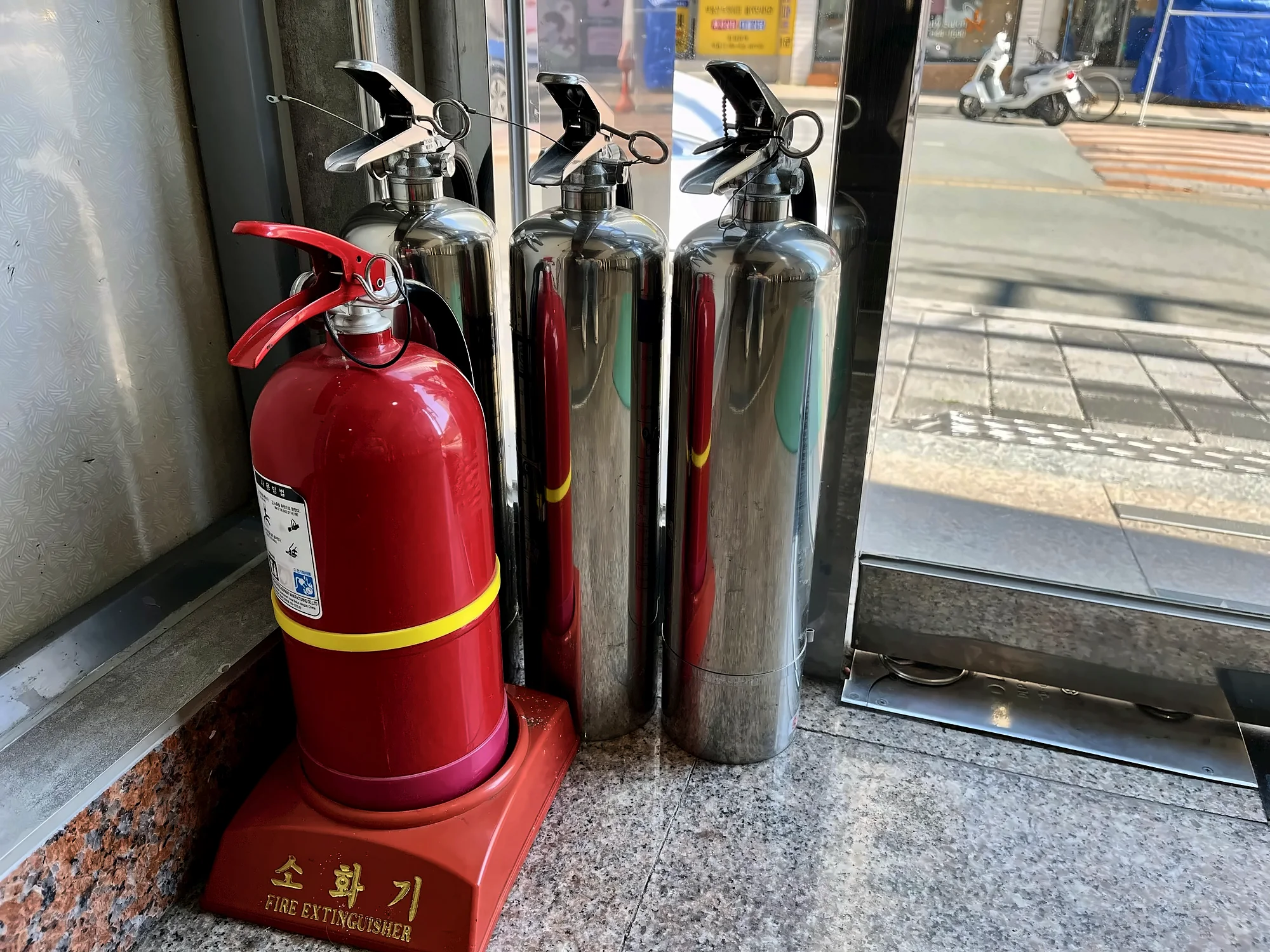입구 옆에 세워 둔 빨간 소화기와 은색 소화기들
