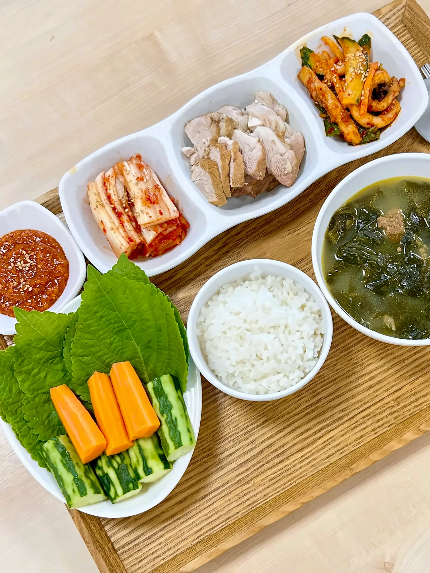 나무 쟁반에 차린 점심. 수육과 깻잎·당근·오이 쌈, 쌈장, 미역국